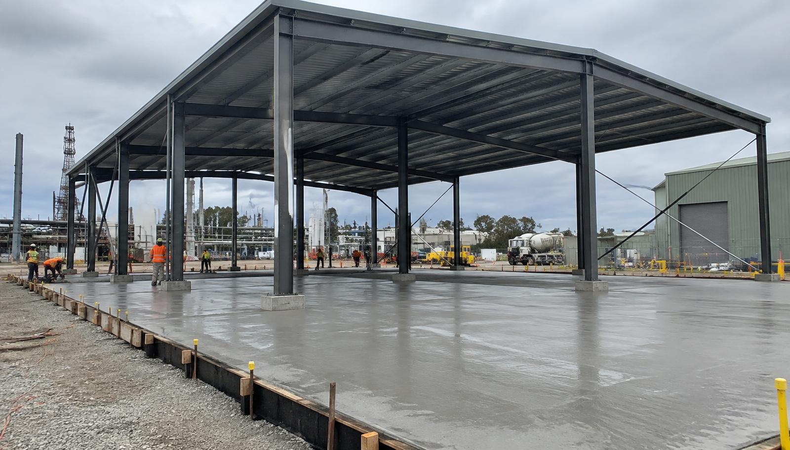 New concrete slab poured beneath a steel-framed overhead industrial shelter
